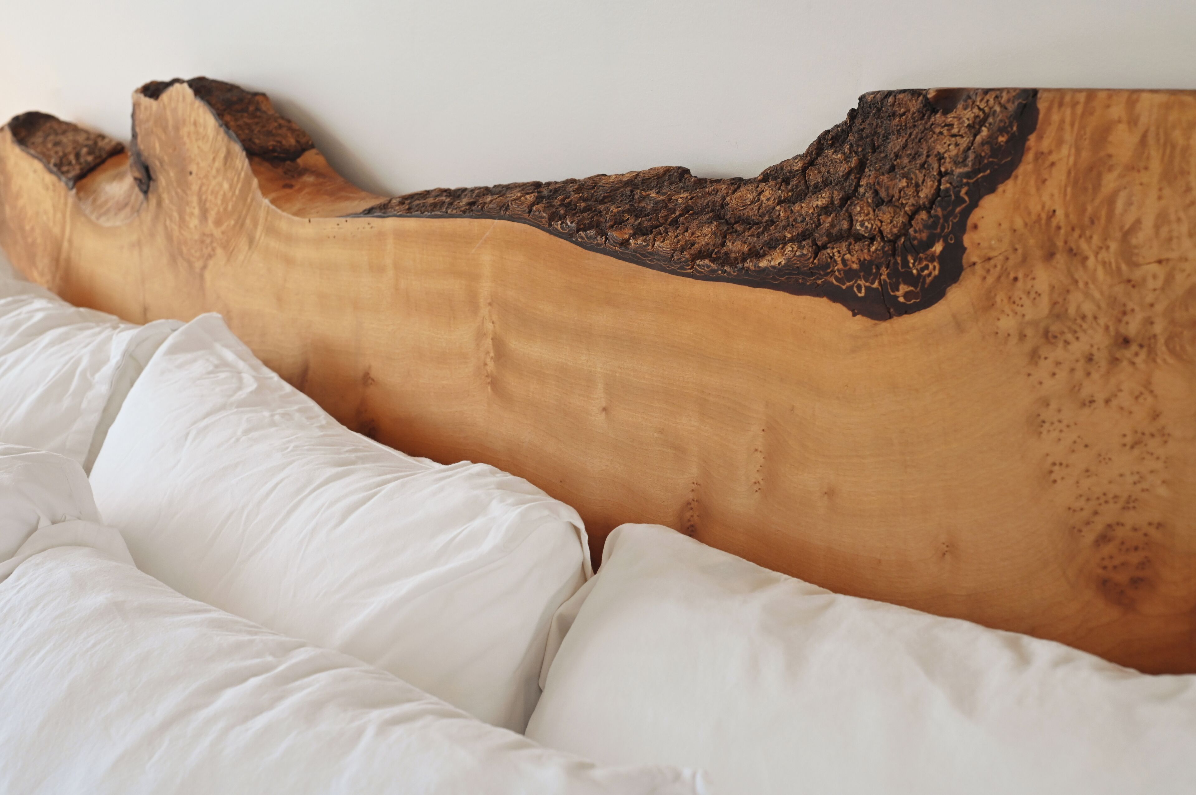 A bed with white bedding and a wooden headboard with a natural wood finish and darkened edges.