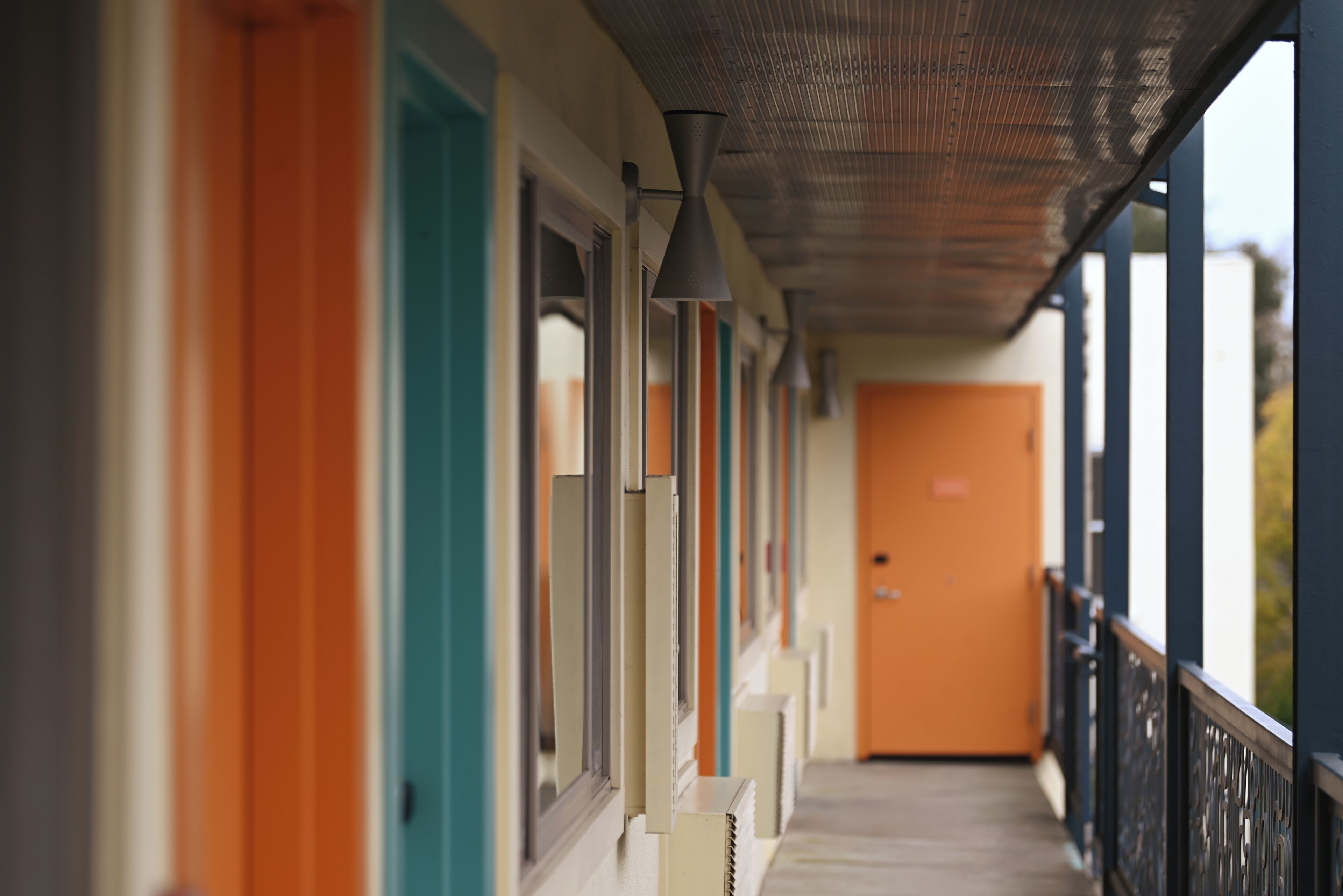 Un corridoio con porte di diversi colori, una ringhiera metallica e una porta in fondo.