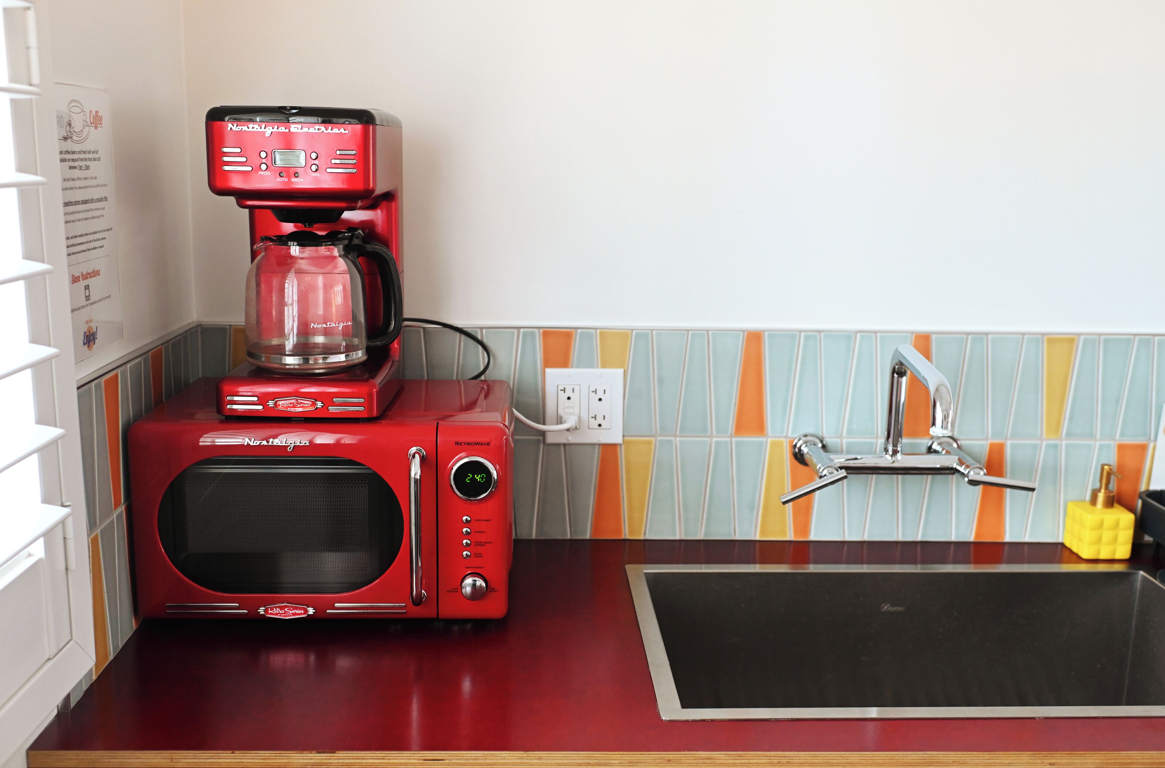 Uma cozinha com micro-ondas vermelho e cafeteira, bancada preta e painel de azulejos.