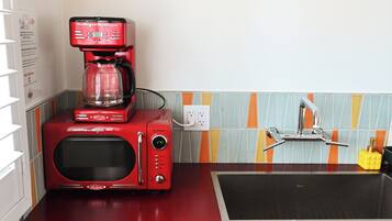 Uma cozinha com micro-ondas vermelho e cafeteira, bancada preta e painel de azulejos.