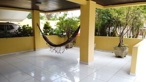 A covered outdoor area with a hammock, tiled floor, yellow walls, and potted plants. - Regina Del Mare Residence (Florianópolis)