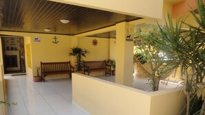 A reception area with a wooden bench, potted plants, and a tiled floor. - Regina Del Mare Residence (Florianópolis)