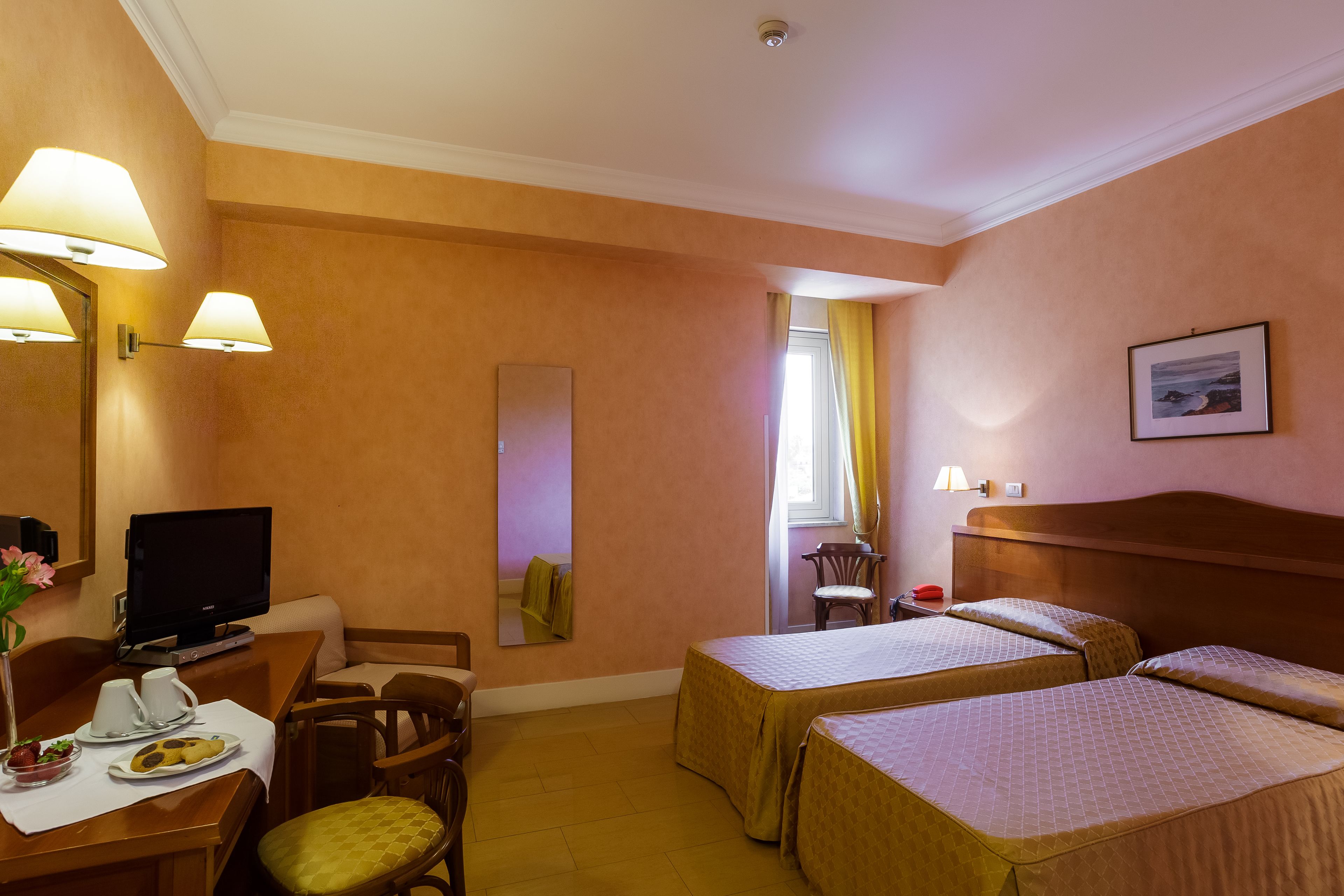 A hotel room with two beds, a desk with a television, a chair, and a dining area with a plate of food.
