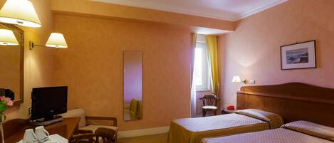 A hotel room with two beds, a desk with a television, a chair, and a dining area with a plate of food.