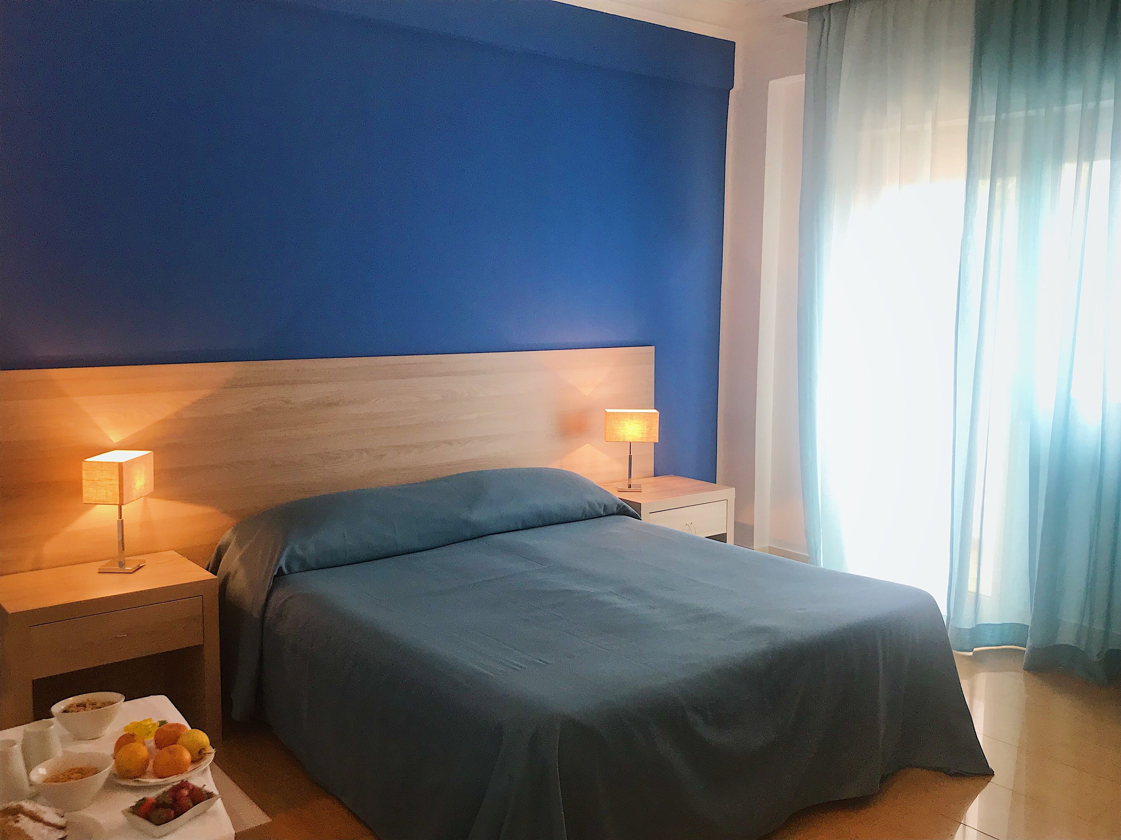 Habitación de hotel con cama, dos mesitas de noche y una bandeja con frutas y cuencos.