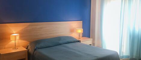Habitación de hotel con cama, dos mesitas de noche y una bandeja con frutas y cuencos.