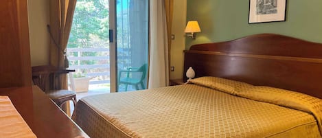 A hotel room with a bed, a desk, a chair, a lamp, and a view of the outdoors.