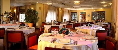 A restaurant with multiple round tables set for dining, each with white tablecloths and red chairs.