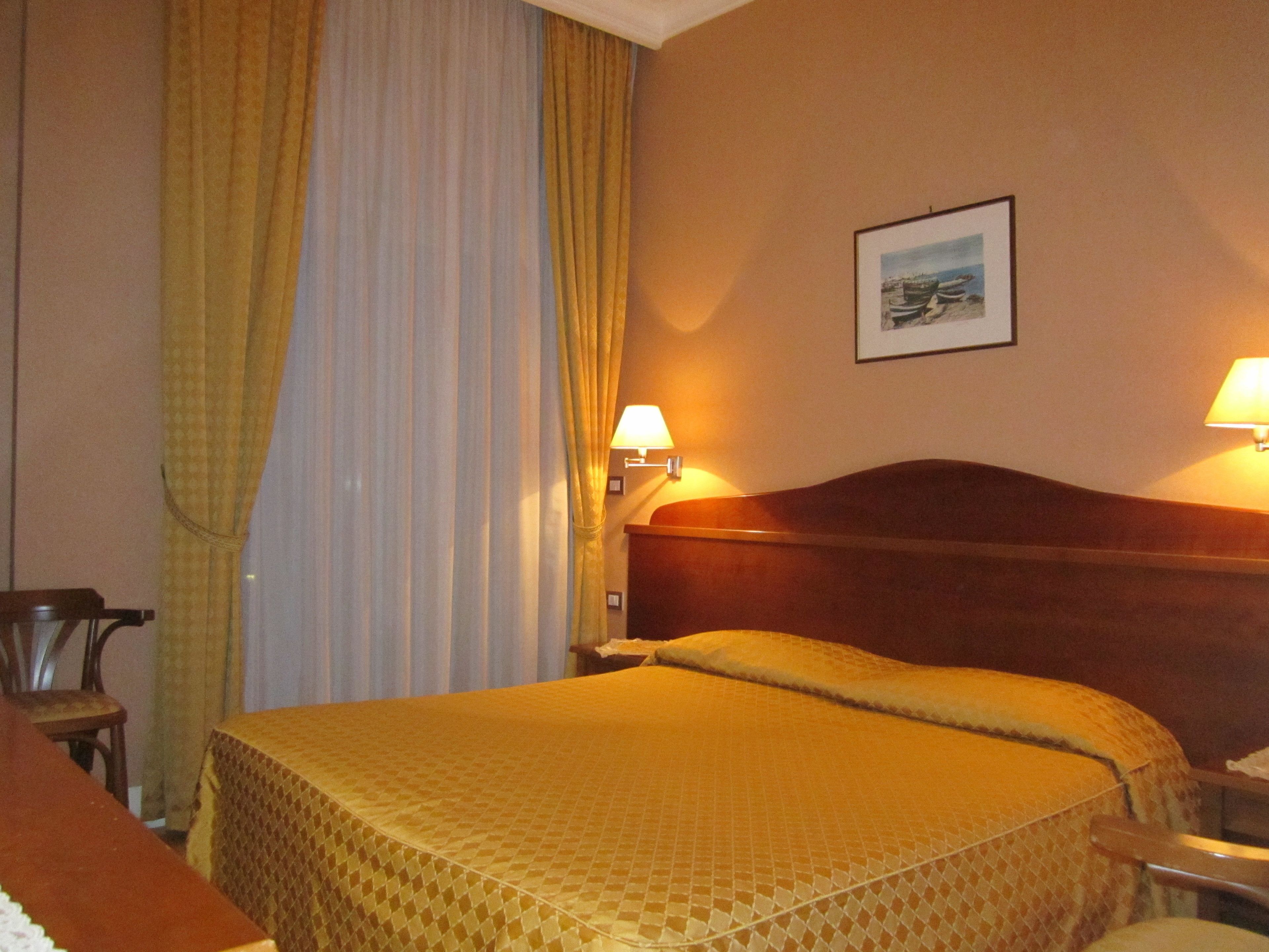 A hotel room with a bed, a nightstand, a lamp, and a framed picture on the wall.