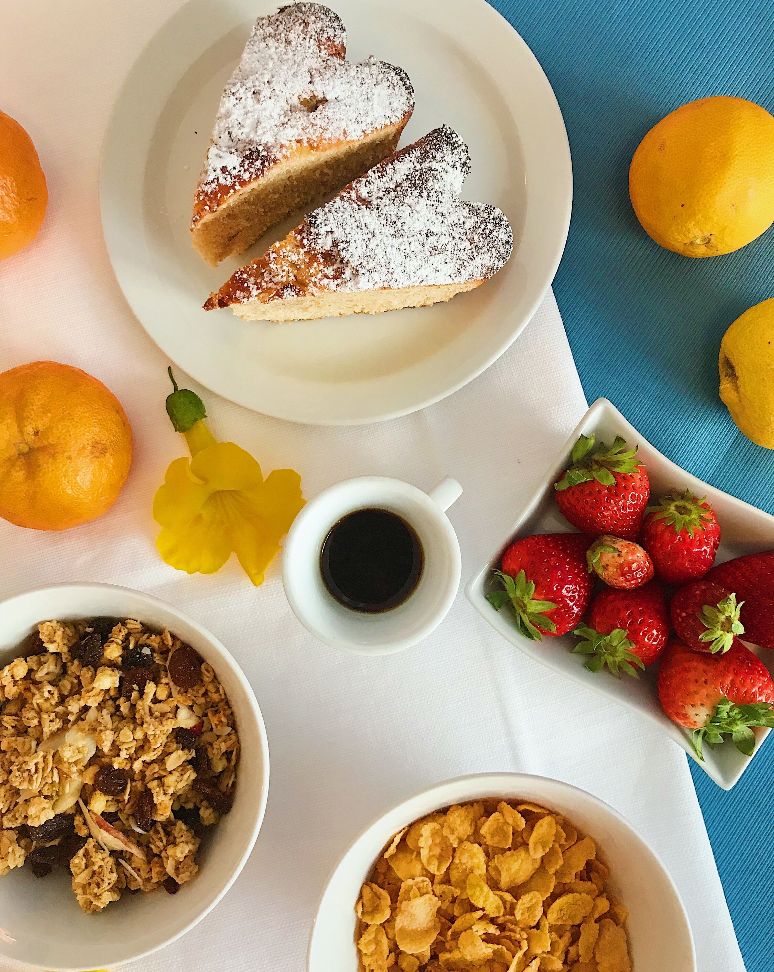 Un desayuno con tostadas francesas, un tazón de granola, un tazón de cereal, una taza de café y una fuente de fresas.