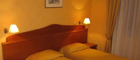 A hotel room with two single beds, a wooden headboard, bedside lamps, a telephone, and a framed picture on the wall.