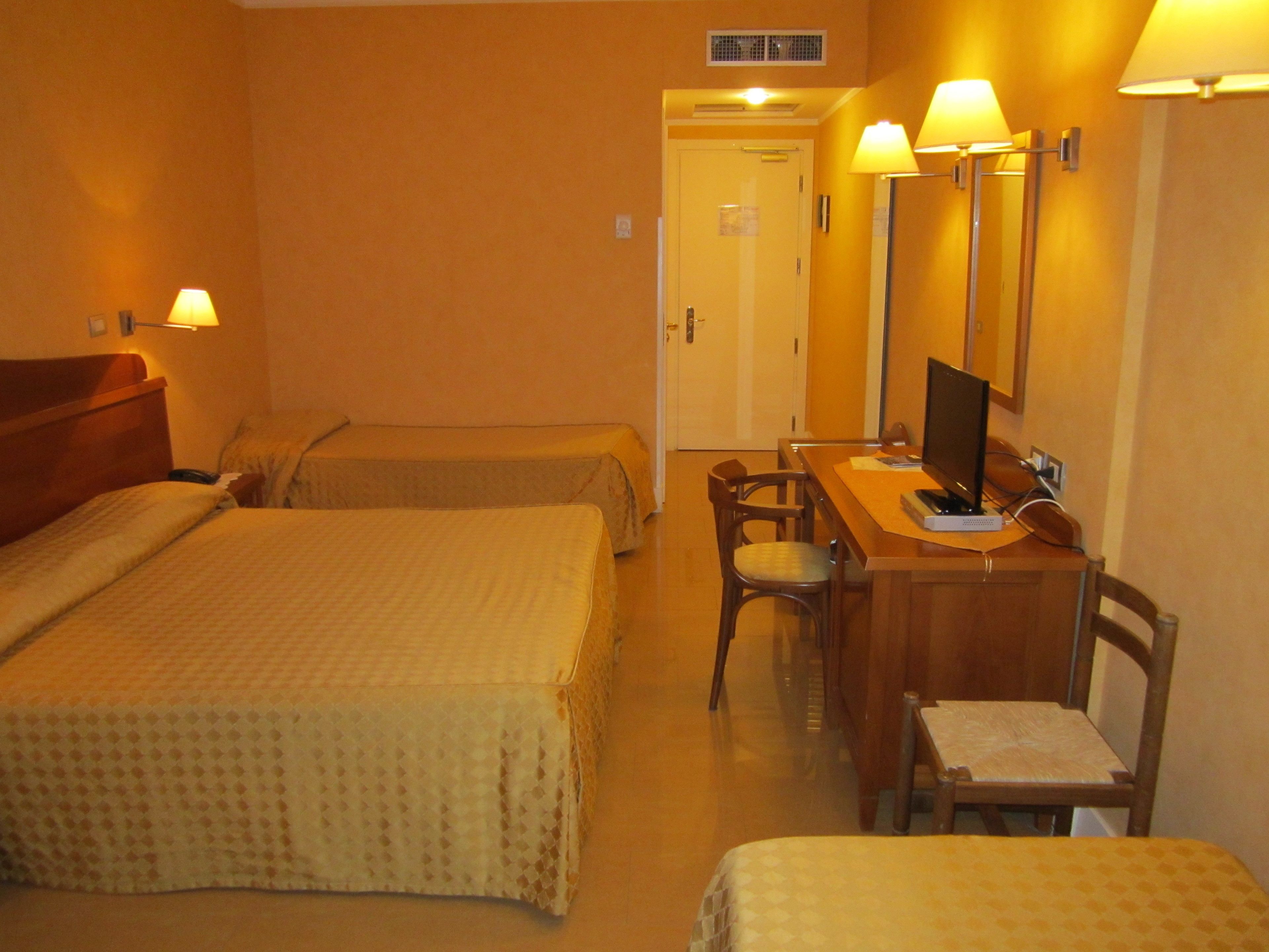 A hotel room with two beds, a desk with a computer, and a chair.