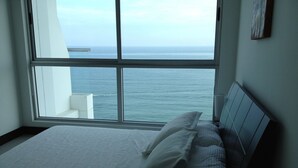 A bedroom with a large window overlooking the sea, a bed with white linens, and a bedside table. - Palmetto Eliptic La Playas Bocagrande (Cartagena)