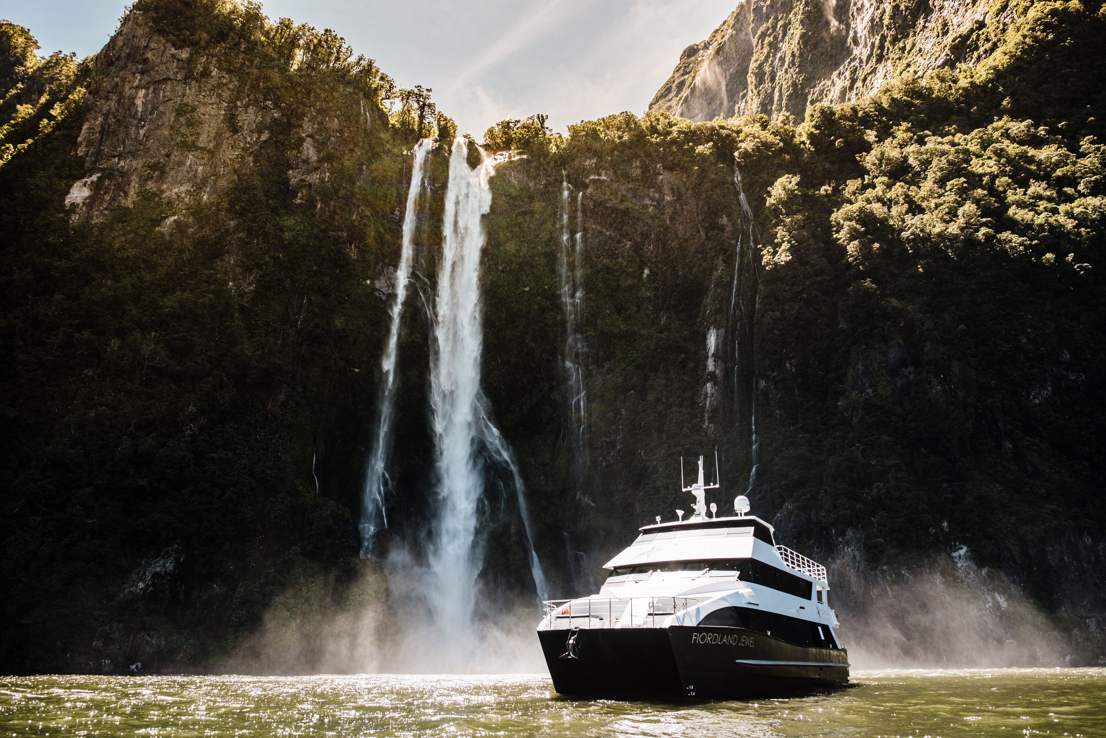 A boat named 'Fjordland' in a body of water with a waterfall in the background.
