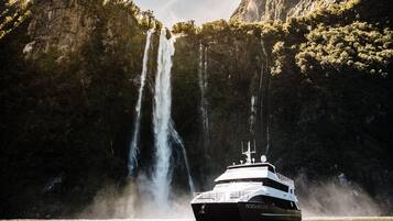 A boat named 'Fjordland' in a body of water with a waterfall in the background.