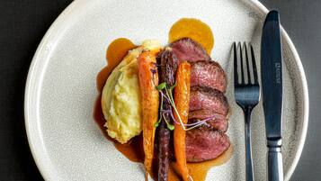 A plate with a steak, carrots, and mashed potatoes, accompanied by a fork and knife on a dark background.