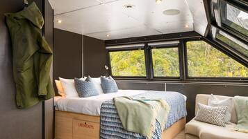 A modern bedroom with a bed, a sofa, and a large window offering a view of greenery.