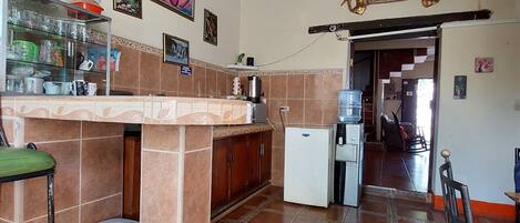 A kitchen with a tiled floor, a refrigerator, a sink, and a counter with various kitchen items.