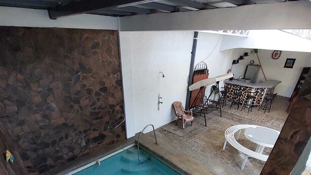 Una piscina con un muro de piedra, un área de bar con taburetes y una pequeña zona de estar.