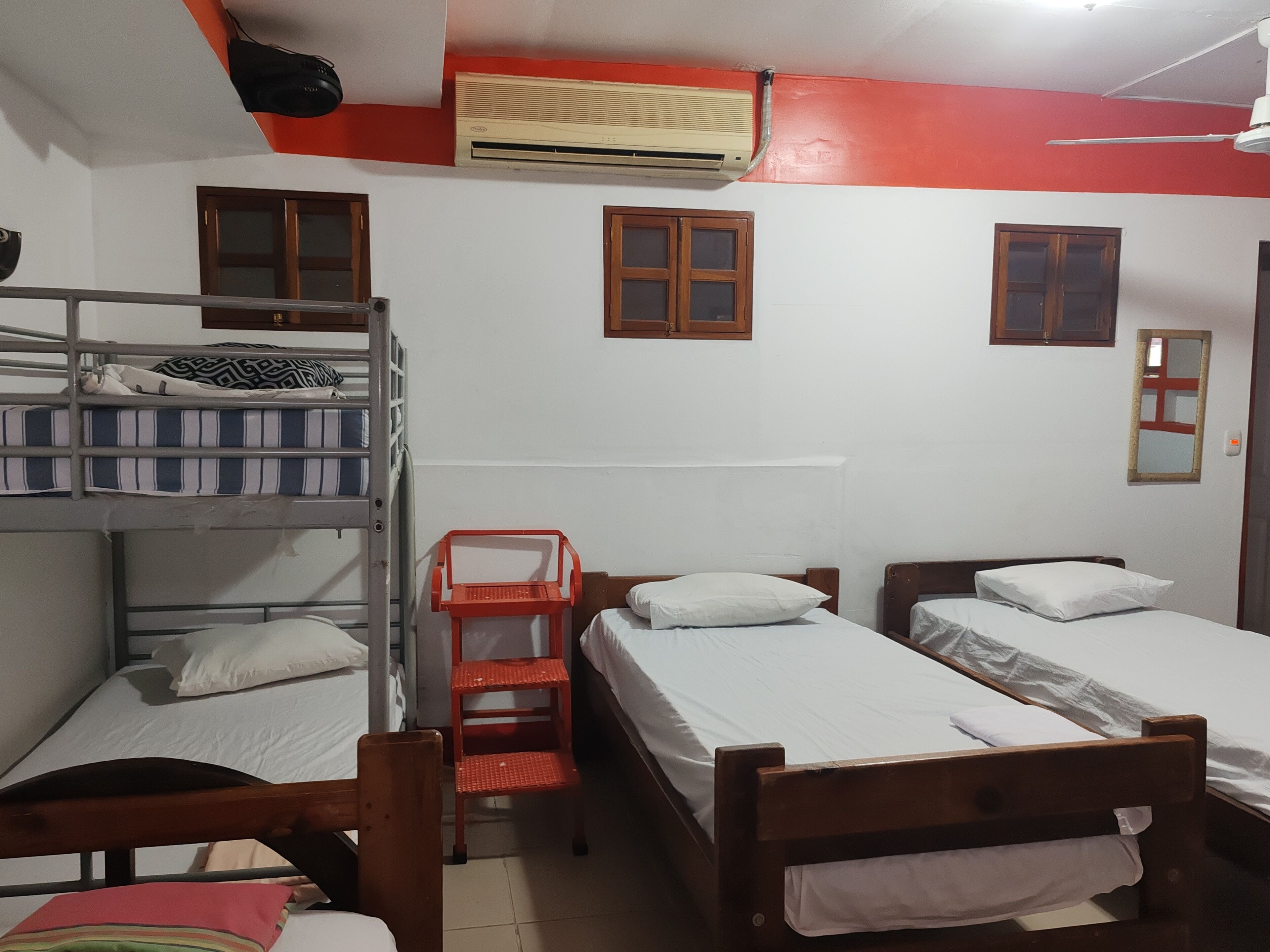Ein Schlafsaalzimmer mit Etagenbetten, einem Einzelbett, einem roten Stuhl und einem Deckenventilator.