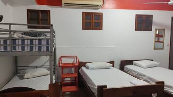 Ein Schlafsaalzimmer mit Etagenbetten, einem Einzelbett, einem roten Stuhl und einem Deckenventilator.