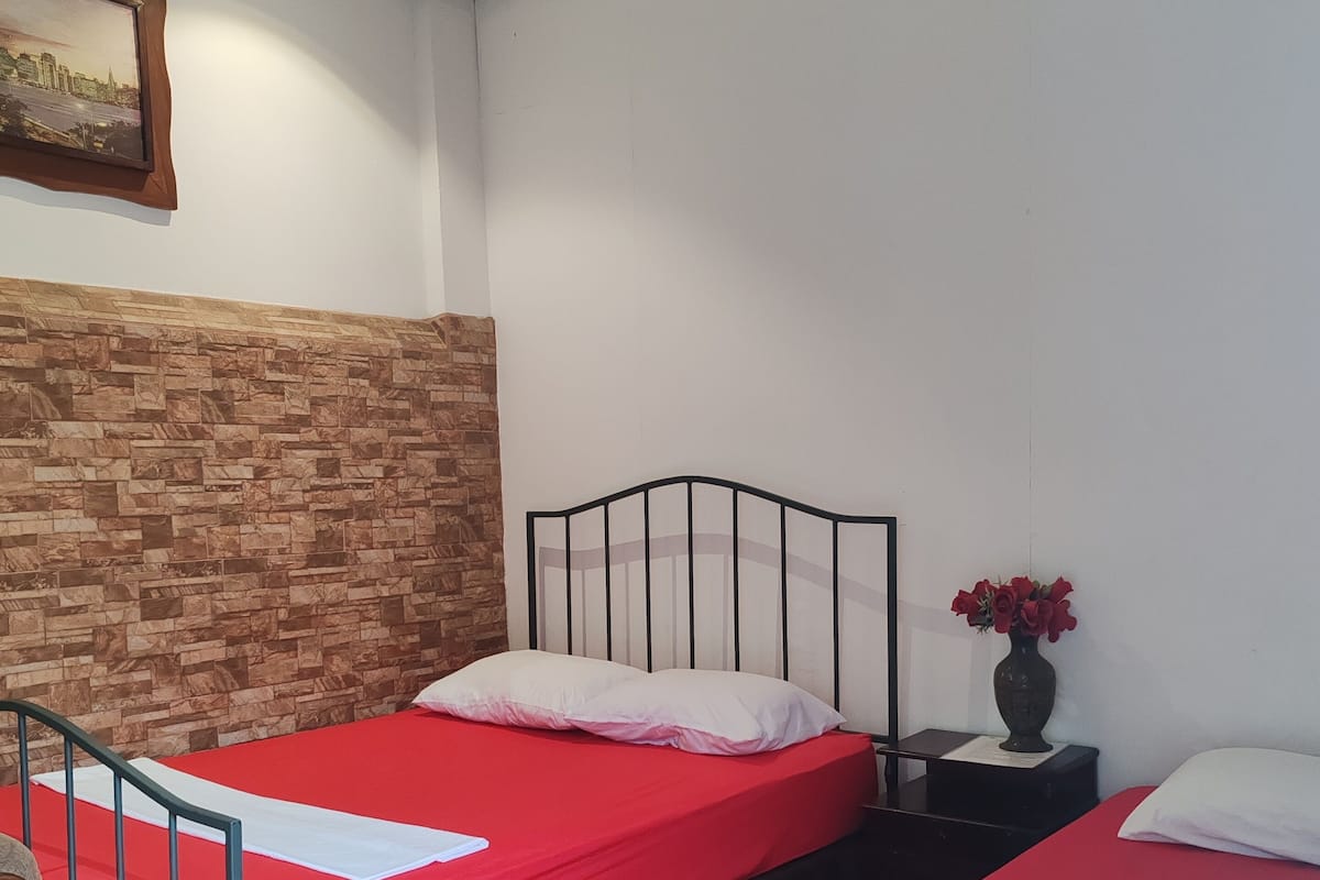 Ein Zimmer mit zwei Betten, einer Holzwand, einem kleinen Tisch mit Blumenvase und einem Bild an der Wand.