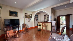 Una sala de estar con televisor, sillas de madera, sofá y piso de baldosas.