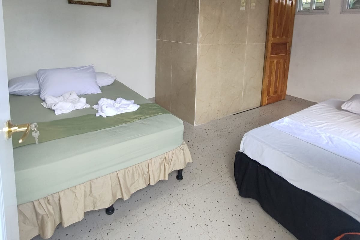 Ein Hotelzimmer mit zwei Betten, einer grünen Bettdecke, einer beigen Wand und einer Holztür.