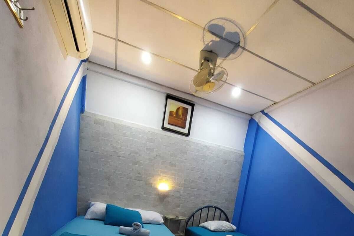 Ein kleiner, kompakter Raum mit zwei Betten, einem Deckenventilator und einer Wandleuchte.