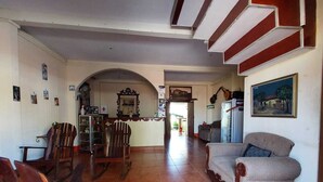 Un amplio salón con suelo de baldosas, una mecedora de madera, un sofá y un refrigerador.