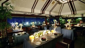 Un restaurant au décor moderne, avec un plafond haut orné de motifs géométriques et de grandes fenêtres offrant une vue sur la ville la nuit.