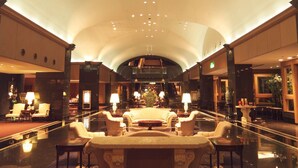 Un hall d’entrée spacieux avec un espace salon central, de nombreuses tables et un plafond haut doté d’un éclairage encastré.