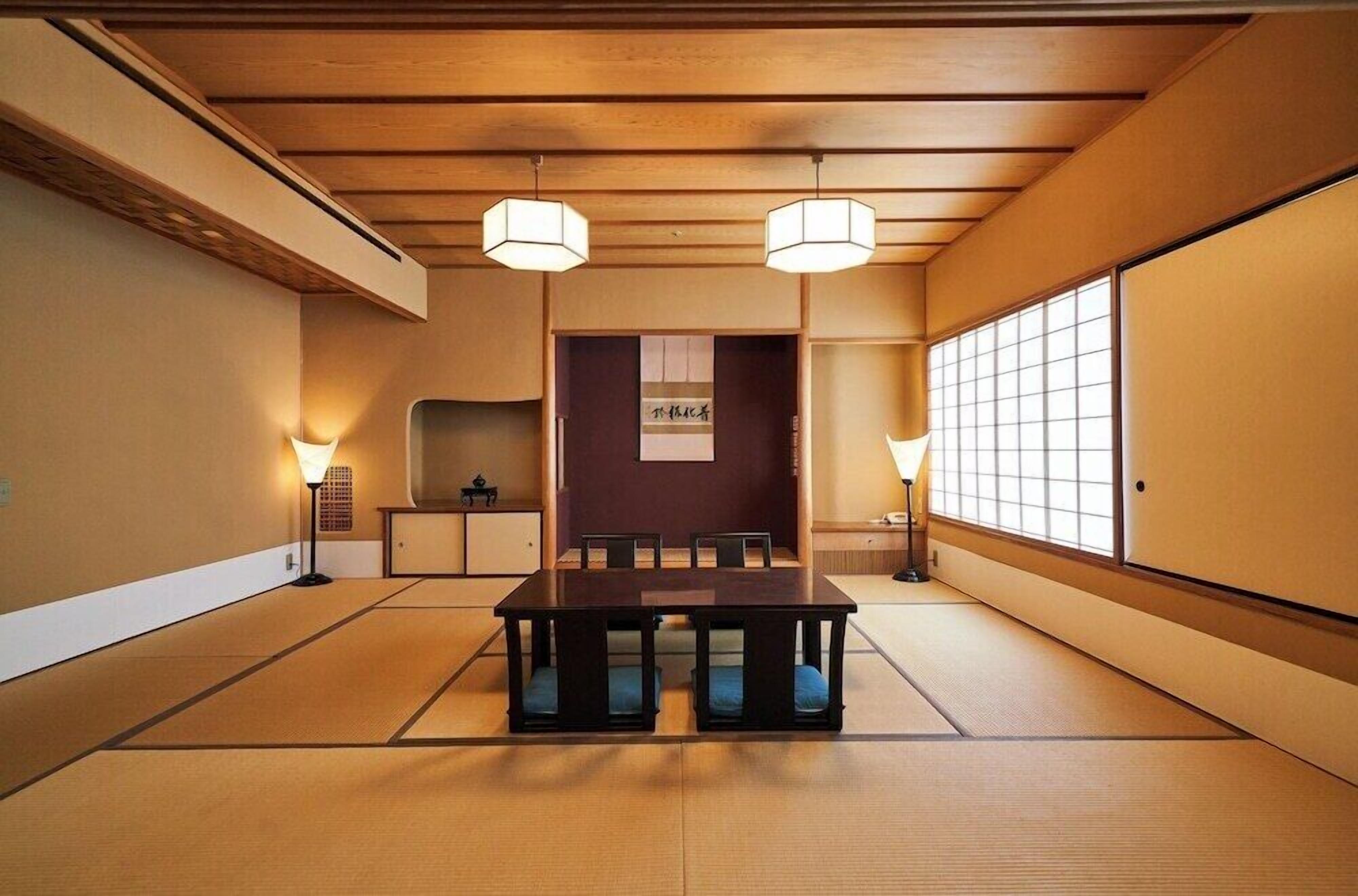A traditional Japanese room with tatami flooring, a low table, and two hanging lamps.