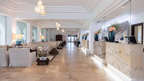 A spacious lobby with a long reception desk, comfortable seating areas, and modern lighting fixtures. - Falkensteiner Resort Capo Boi (Villasimius)