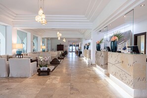 A spacious lobby with a long reception desk, comfortable seating areas, and modern lighting fixtures. - Falkensteiner Resort Capo Boi (Villasimius)