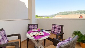 A balcony with wicker chairs, a small table, and a view of a hilly landscape. - Apartments Mira (Dubrovnik)