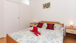 A bedroom with a bed, two bedside tables, a nightstand, a window, and a wall-mounted picture. - Apartments Mira (Dubrovnik)