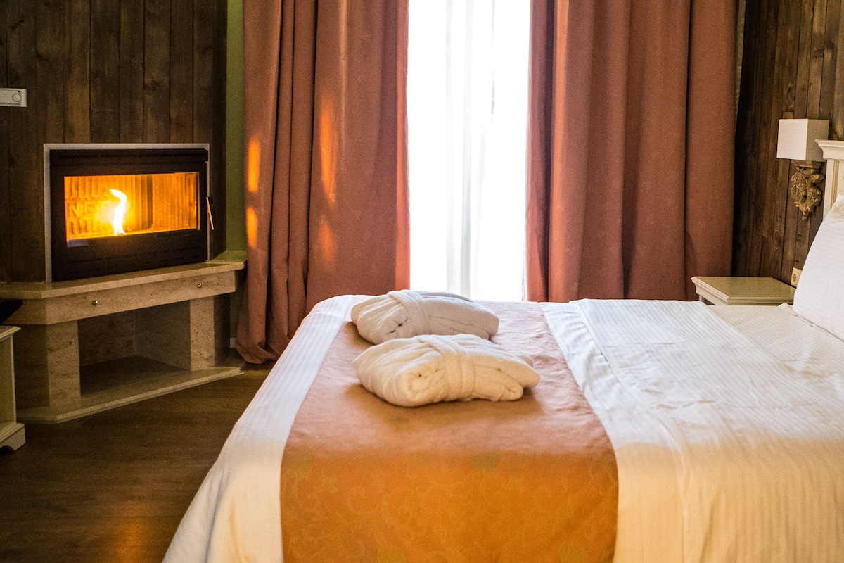 A hotel room with a bed, a bedside table with a lamp, a wooden wall, and a fireplace.