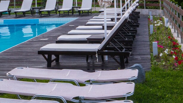 A poolside area with lounge chairs and umbrellas, surrounded by greenery and mountains.
