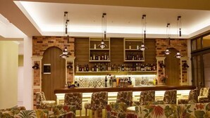 A bar area with a brick wall, shelves of bottles, and a counter. There are floral-patterned chairs and hanging pendant lights.