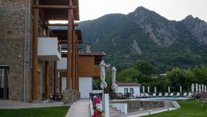 A modern building with a stone facade, a covered outdoor area with seating, and a view of mountains in the background.