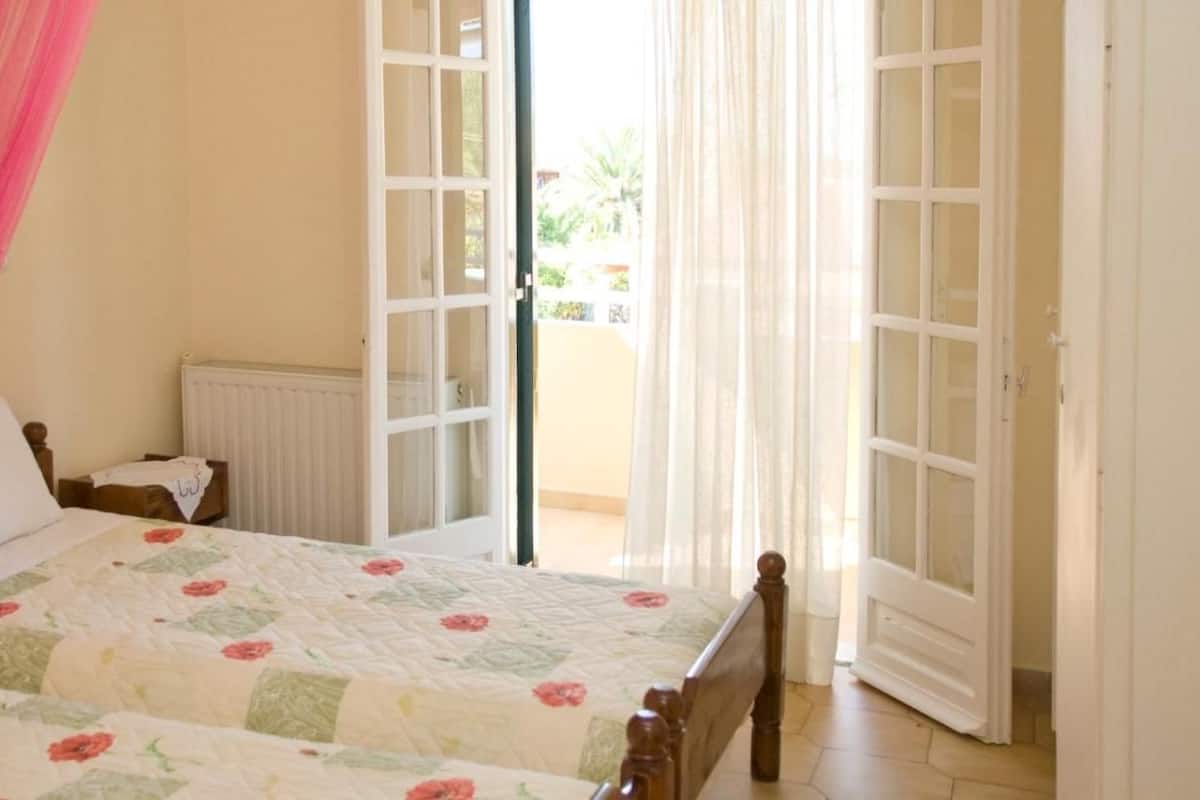 A bedroom with two beds, a radiator, and a view of the outdoors through a door.
