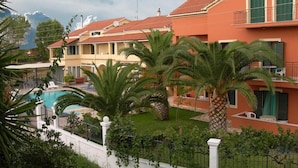 Un edificio residencial con piscina, rodeado de palmeras y un césped cuidado.