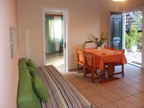A dining area with a table covered in an orange tablecloth, wooden chairs, and a bench with green cushions. - Katerina Pool Apartments (Corfu)