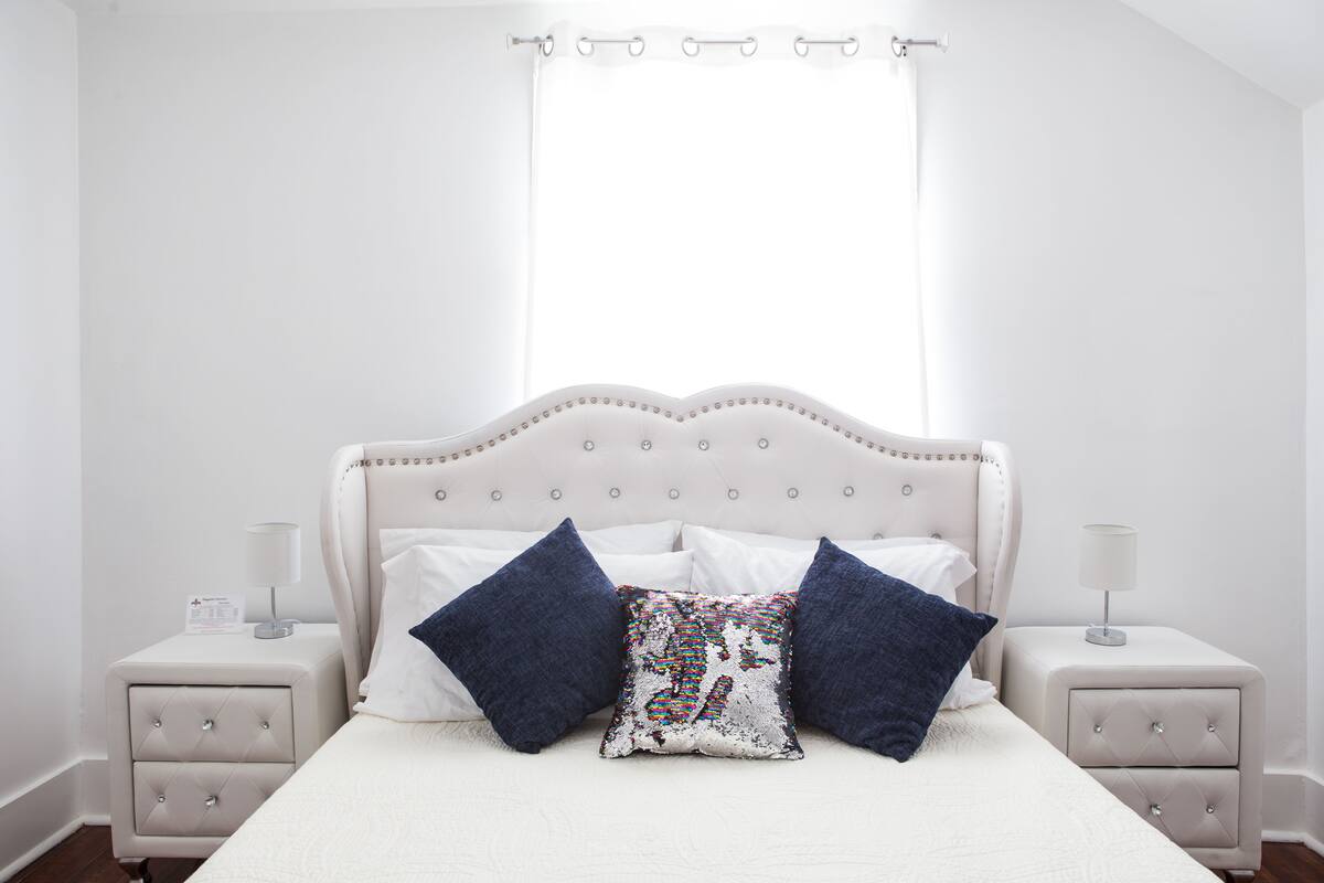 A neatly arranged bedroom with a large bed, two bedside tables, and a window with curtains.