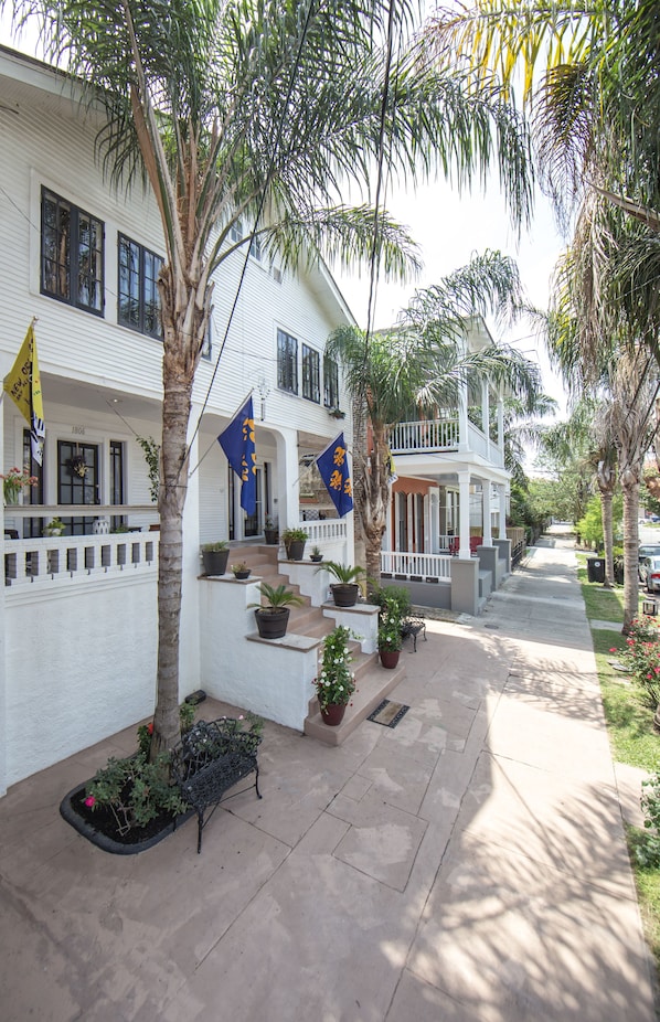 A white two-story house with a porch, palm trees, and flags.