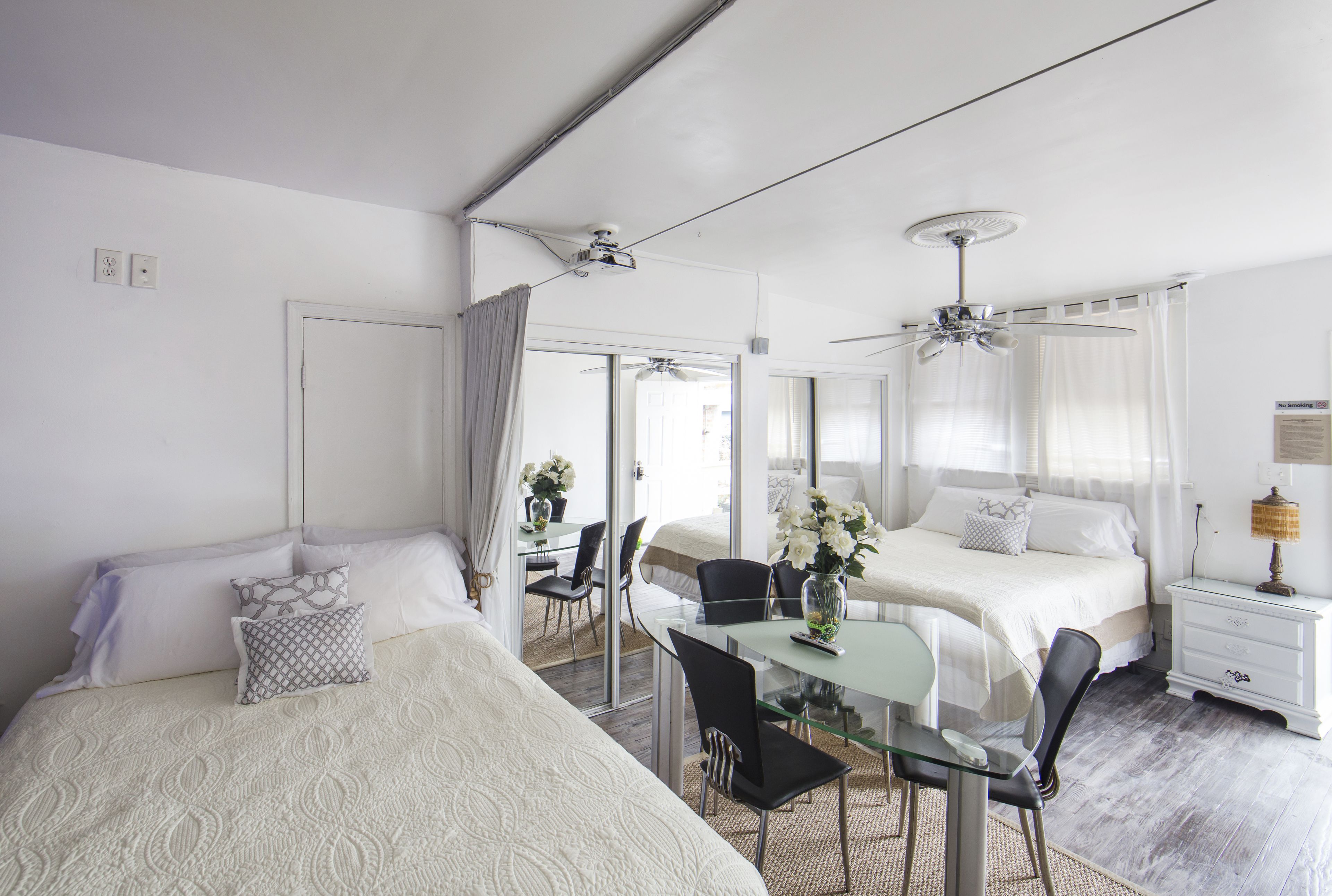 A bedroom with two beds, a glass dining table, and ceiling fans.