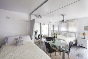 A bedroom with two beds, a glass dining table, and ceiling fans.