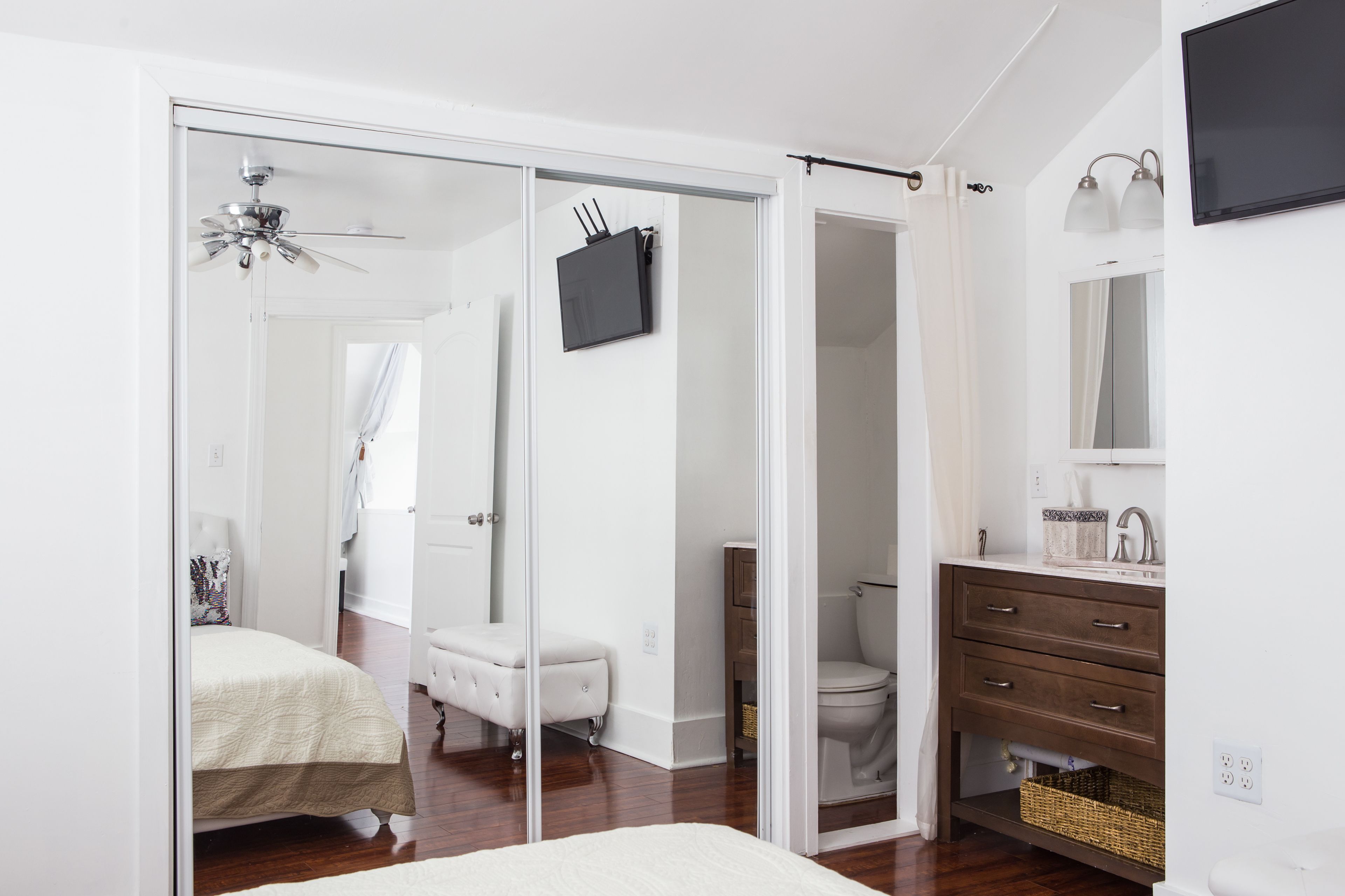 A bedroom with a bed, a white wardrobe, a bathroom with a toilet and sink, and a TV mounted on the wall.