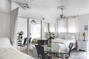 A hotel room with a glass dining table, two black chairs, a bed with white bedding, a ceiling fan, and a nightstand with a lamp. - Magazine Mansion (New Orleans)